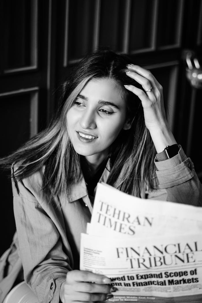 services-02 Black and white portrait of a woman reading Tehran Times newspaper, touching her hair.