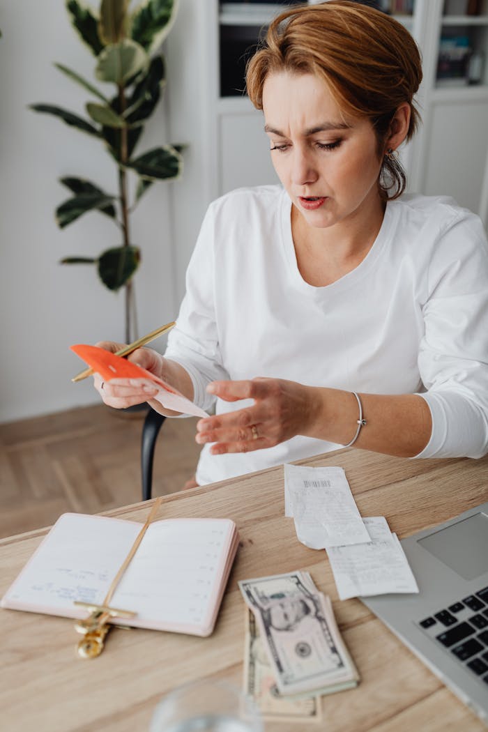 services-04 Woman calculating expenses with calculator and notebook at home office, surrounded by receipts and money.